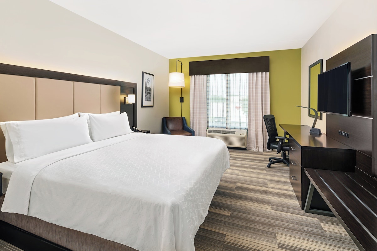 A hotel room with a large bed, a desk with a chair, a television, and a window with curtains.