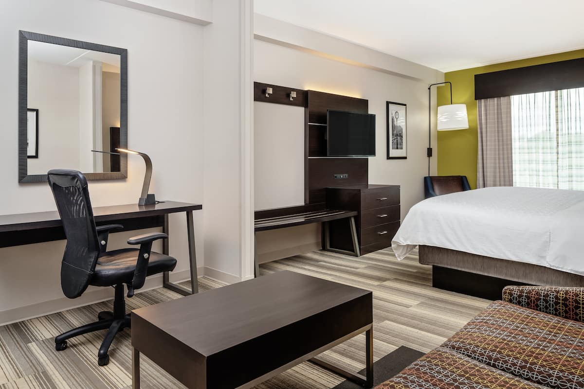 Een hotelkamer met een bed, bureau, stoel, televisie en een grote spiegel.