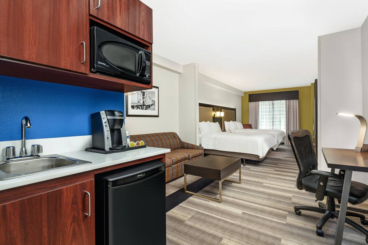 Een hotelkamer met een kitchenette, een bed, een slaapbank, een bureau en een stoel.