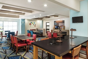 A hotel lobby with a seating area, a coffee station, and a TV mounted on the wall.