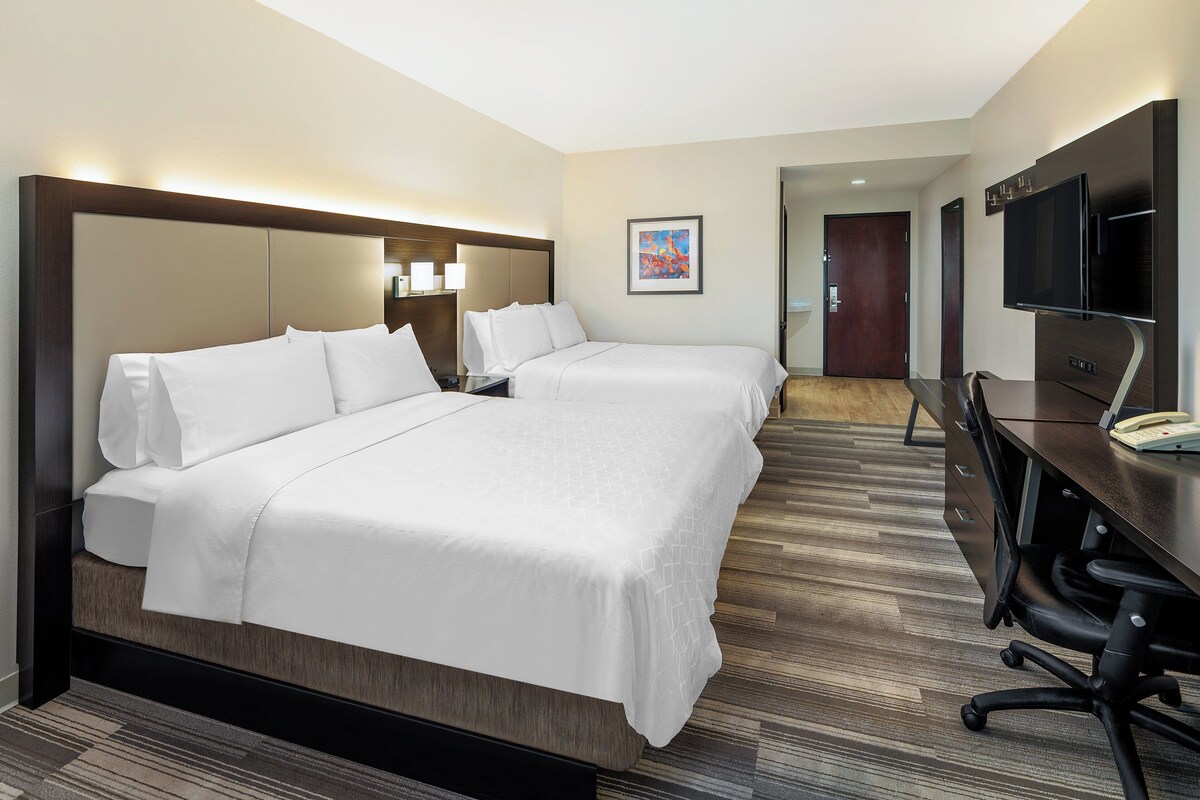 A hotel room with a large bed, bedside tables, a desk with a chair, a flat-screen TV, and a framed picture on the wall.