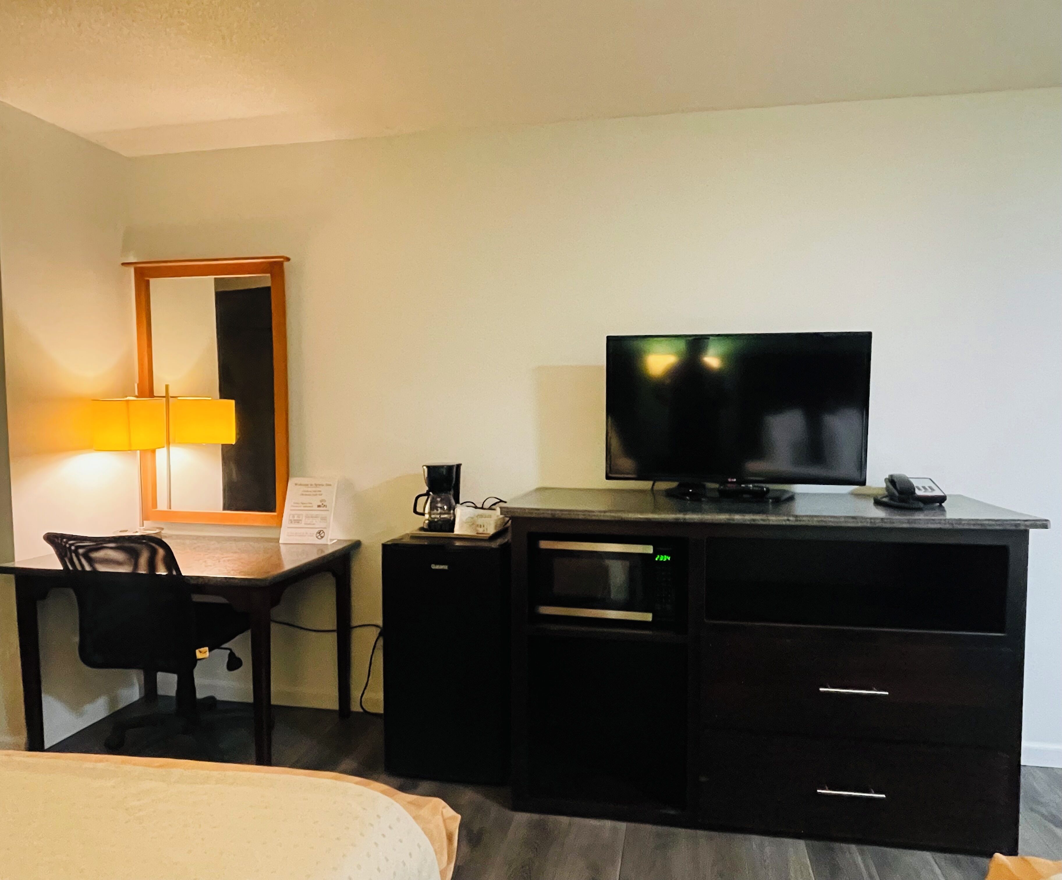 A hotel room with a bed, a desk with a television, a coffee maker, and a lamp.