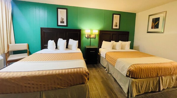 A hotel room with two beds, a chair, a nightstand, and wall-mounted lamps. - Sparta Inn (Sparta)