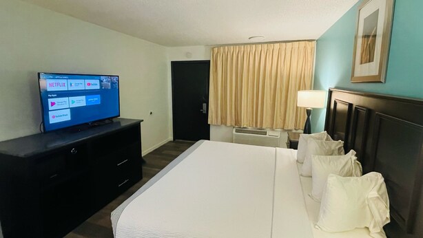 Habitación de hotel con cama, televisión en una cómoda, escritorio, silla, lámpara y puerta.