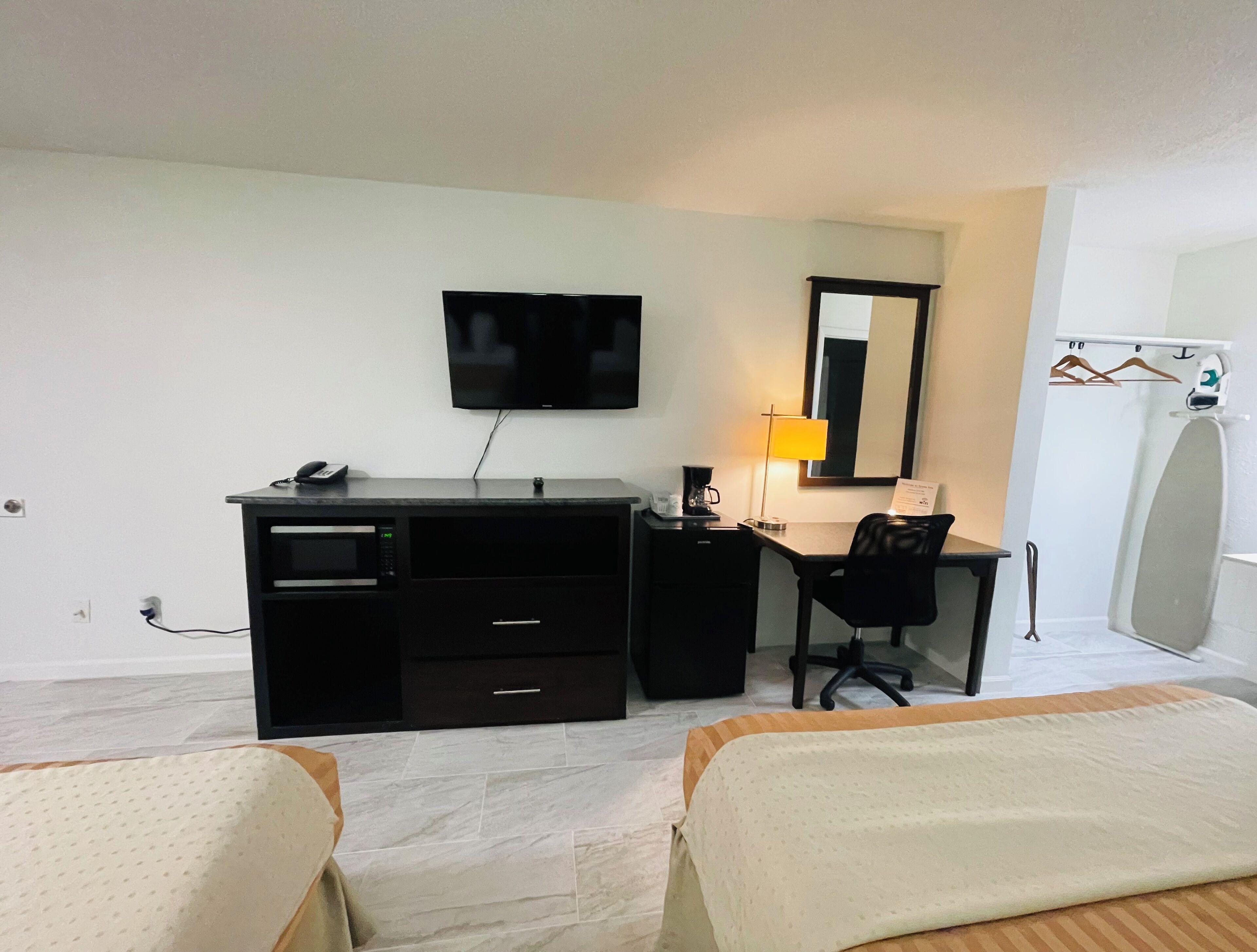 A hotel room with a bed, a desk, a chair, a television, a lamp, and a mirror.