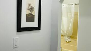 A hallway with a framed picture on the wall, a light switch, and a bathroom visible through an open door.