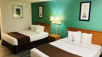 A hotel room with two single beds, a nightstand with a lamp, and framed pictures on the walls.