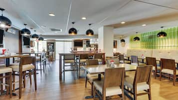 Een restaurant met houten tafels en stoelen, een bar en een groene accentmuur.