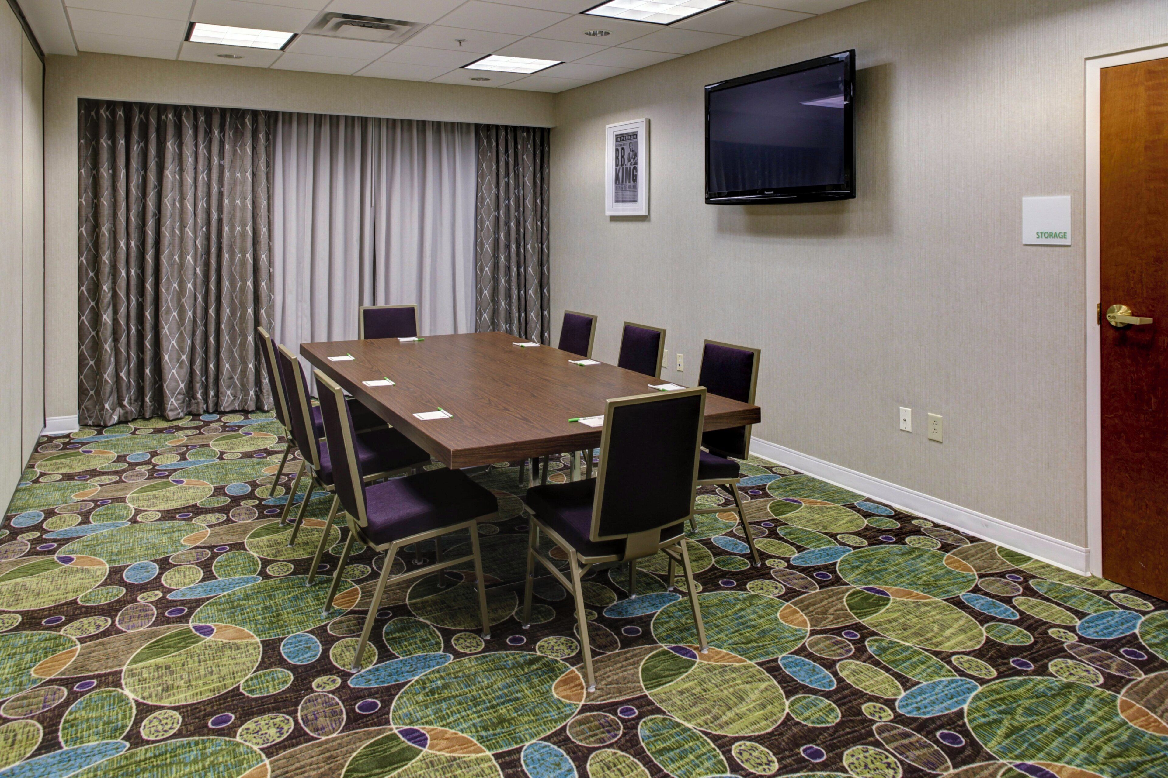 A conference room with a large table, chairs, a television, and a patterned carpet.