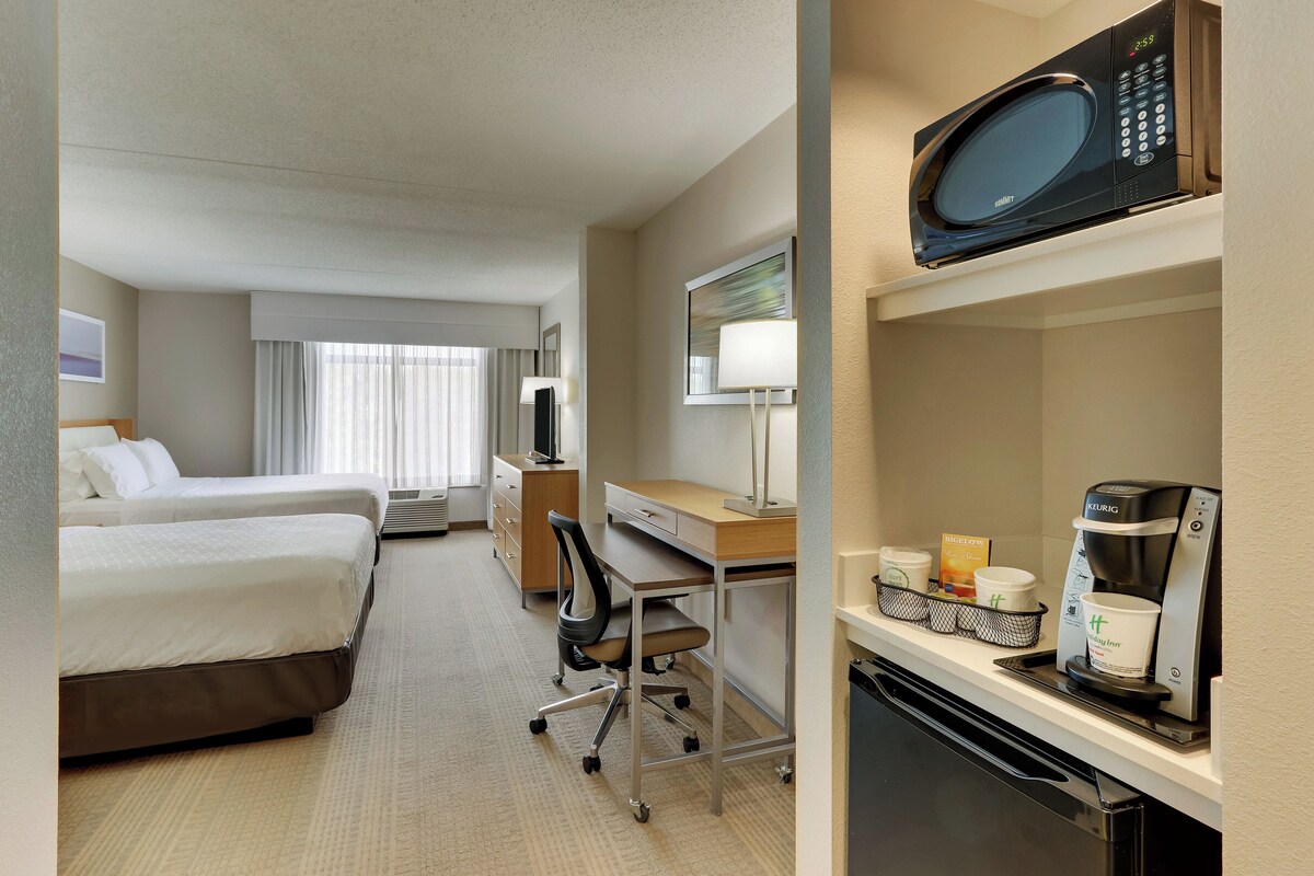 Habitación de hotel con dos camas, un escritorio con silla, microondas, cafetera y refrigerador pequeño.