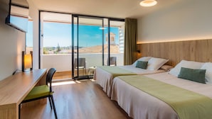 A hotel room with two beds, a desk, and a chair. There is a large window with a view of a building and a landscape.