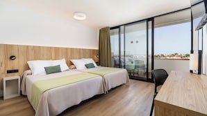 A modern hotel room with two beds, a desk, and a large sliding glass door to the balcony.