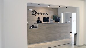 A reception desk with two HP monitors, a sign with a sun and exclamation mark, and a woman standing behind it.