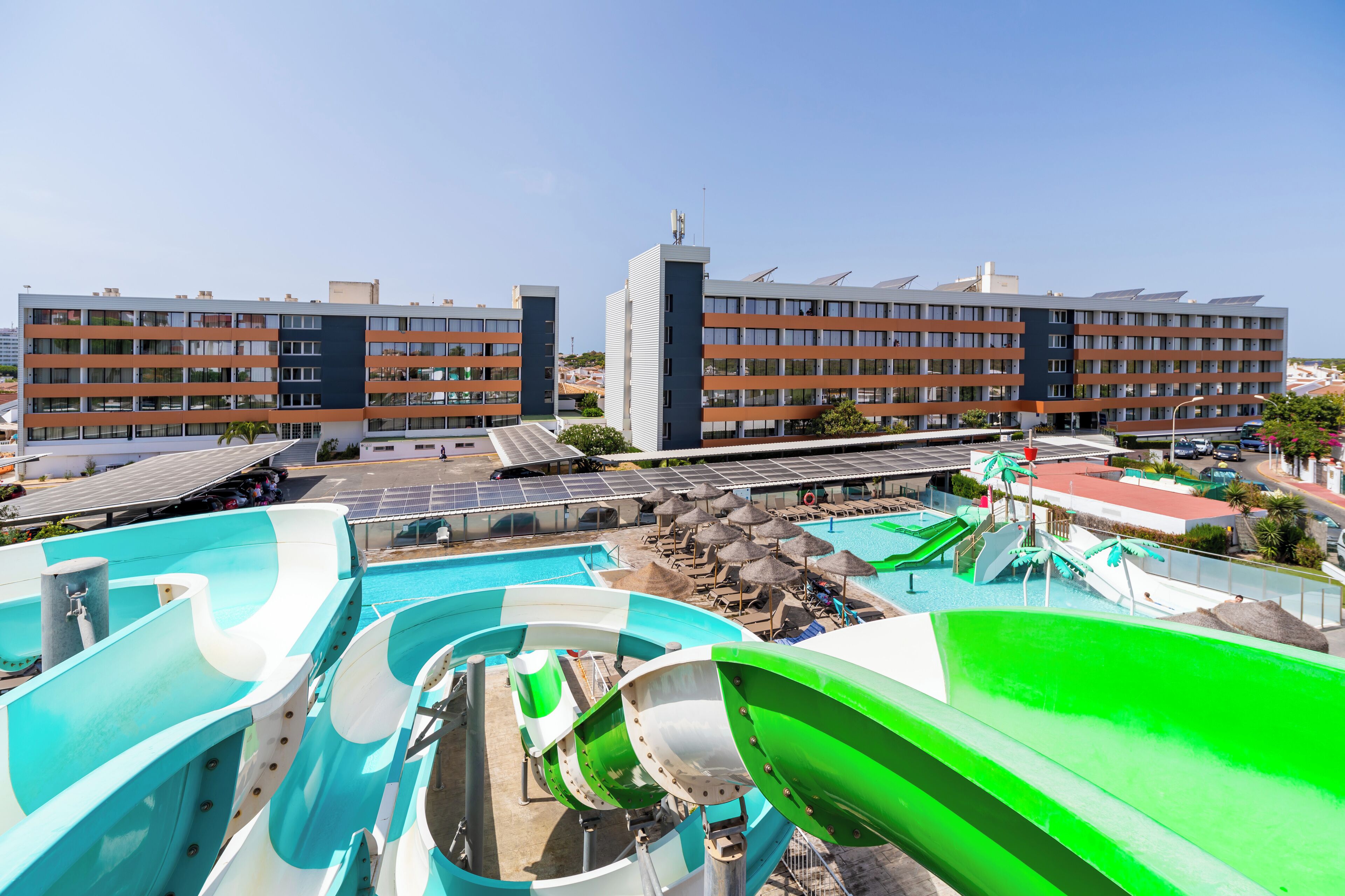 Un hotel con varias piscinas, un tobogán acuático y un edificio grande con balcones.
