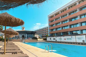 A hotel pool area with sun loungers and umbrellas, a swimming pool, and a building with multiple balconies. - Ohtels Carabela (Almonte)