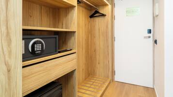 Una habitación pequeña con un armario de madera, una caja fuerte negra y una puerta blanca con un aviso.