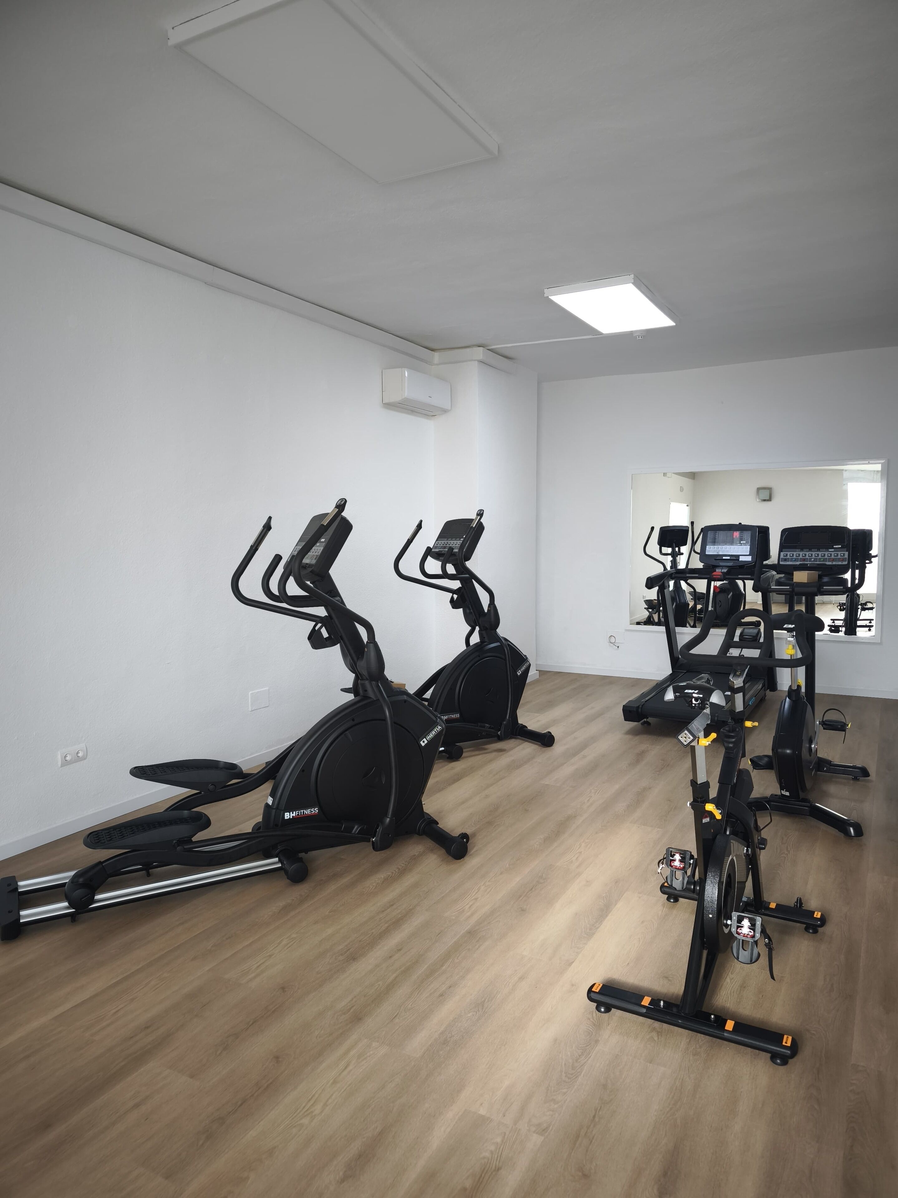 Un gimnasio con bicicletas estáticas, cintas de correr y un equipo de aire acondicionado en la pared.