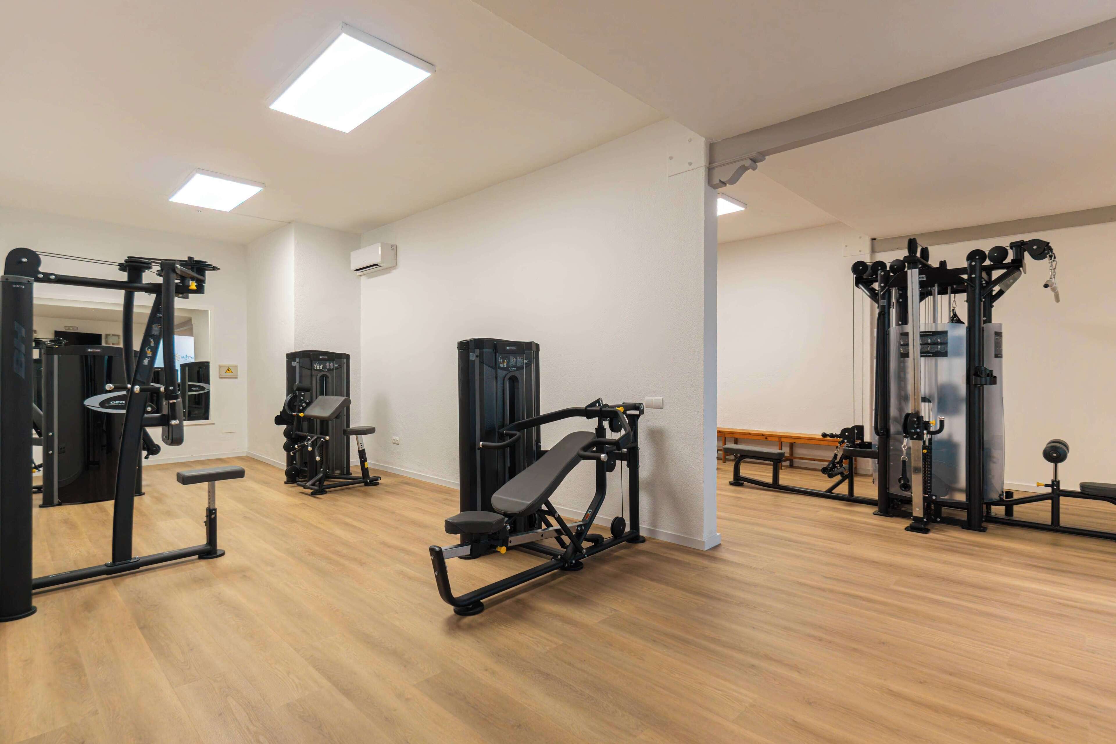 Una palestra con diverse attrezzature per esercizi, pavimento in legno e pareti bianche.