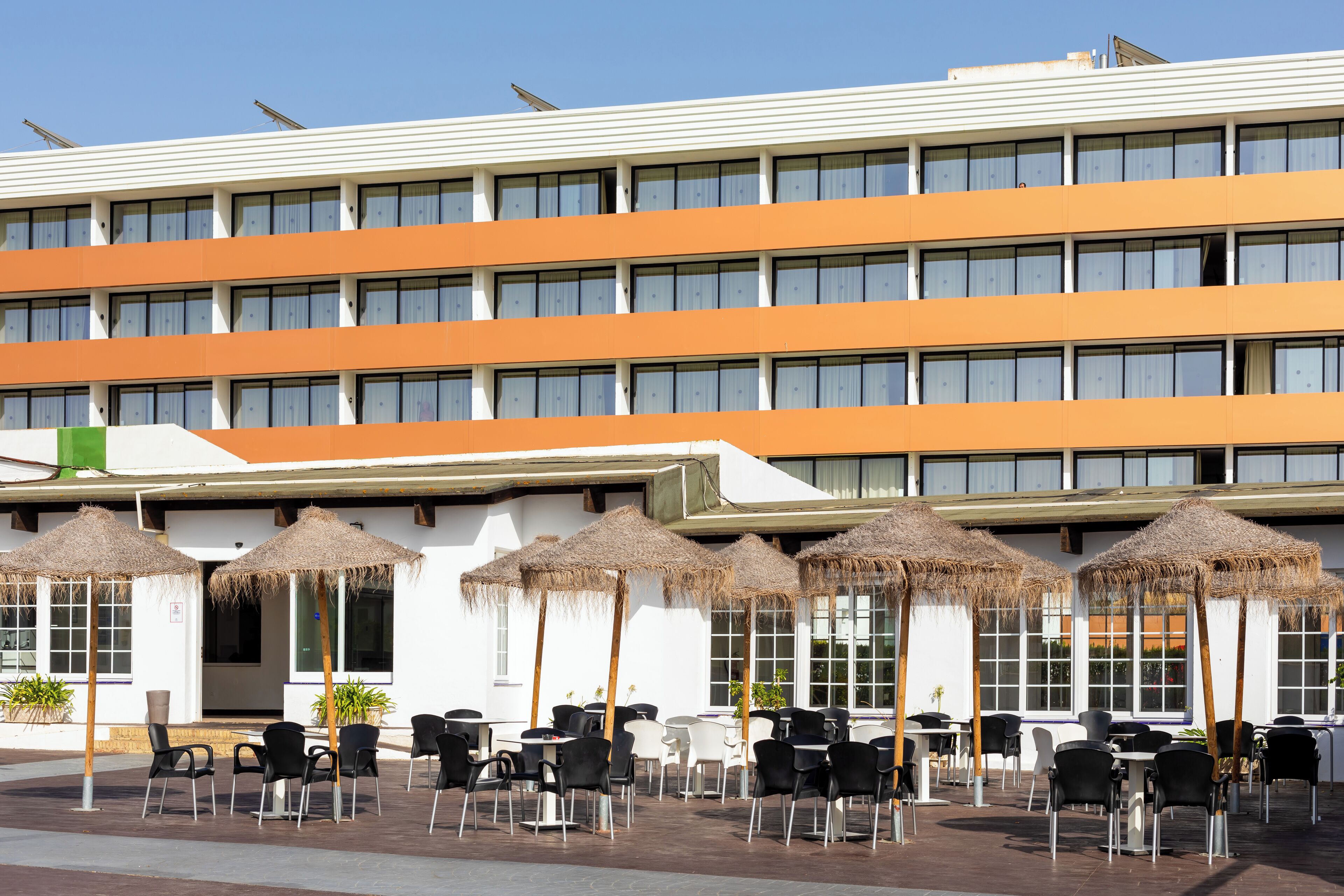 Un hotel con terraza al aire libre y sombrillas, fachada blanca y varias ventanas.