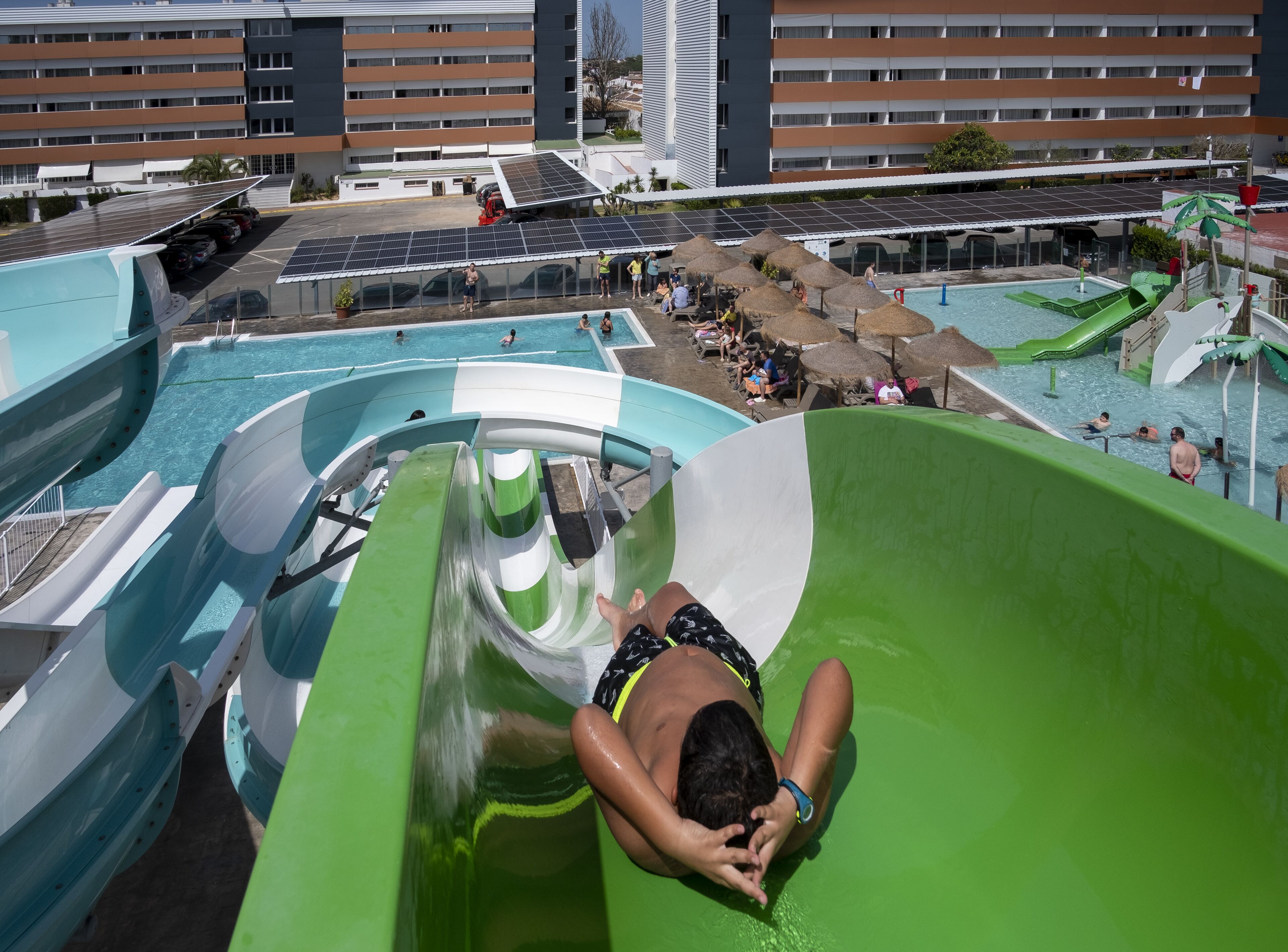Un tobogán de agua en un complejo turístico con zona de piscina y un edificio al fondo.