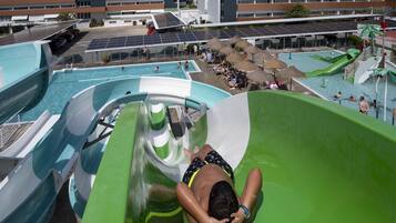 Un tobogán de agua en un complejo turístico con zona de piscina y un edificio al fondo.