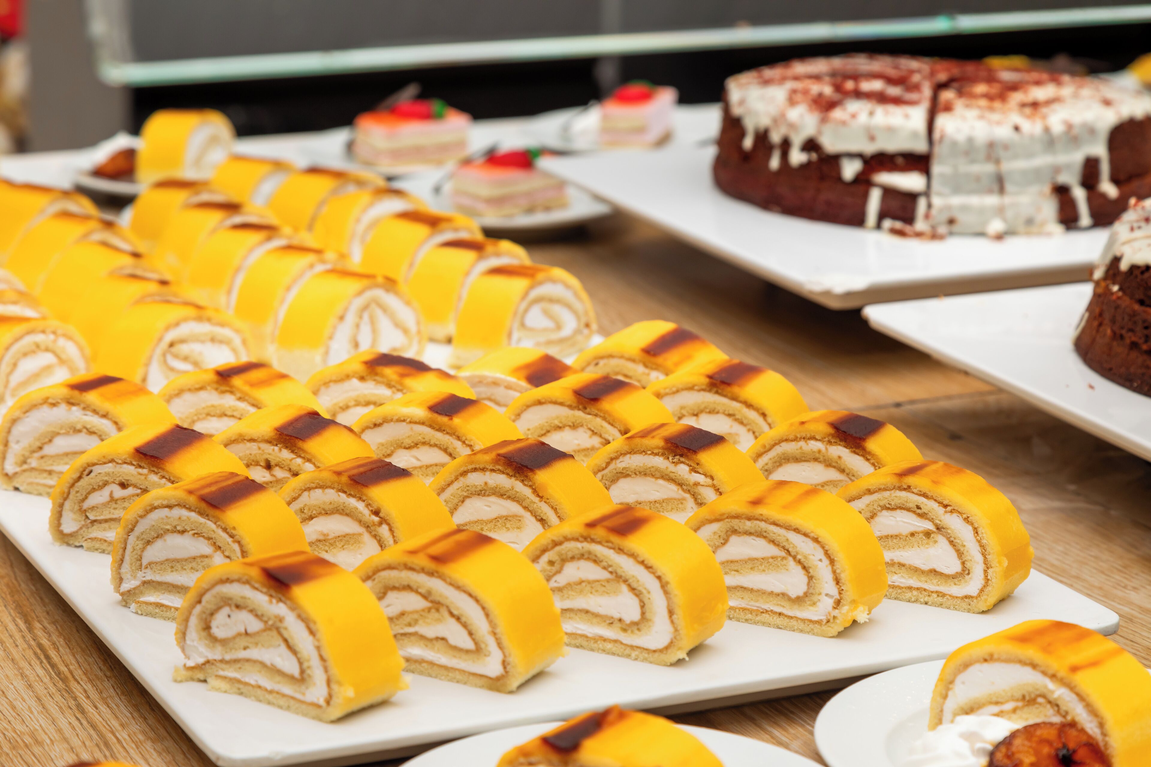Variedad de postres en platos blancos, incluyendo un pastel grande de chocolate con cobertura blanca y un pastel más pequeño con un topping rojo.