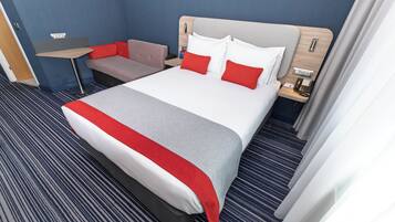 Una habitación de hotel con una cama grande, un escritorio pequeño, un sofá y una mesita de noche con un teléfono.