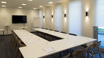 Una sala de conferencias con una larga mesa, sillas, una pizarra y una pantalla de proyector.