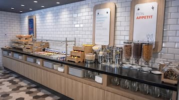 Zona de bufé con diversas opciones de comida y un cartel que indica el horario de desayuno.