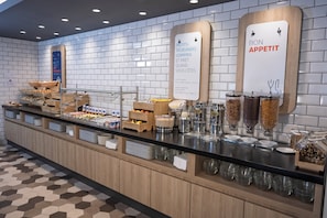 Zona de bufé con diversas opciones de comida y un cartel que indica el horario de desayuno.