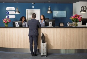 A hotel reception desk with a digital display, a clock, and a sign for Holiday Inn Express. - Holiday Inn Express Geneva Airport by IHG (Meyrin)