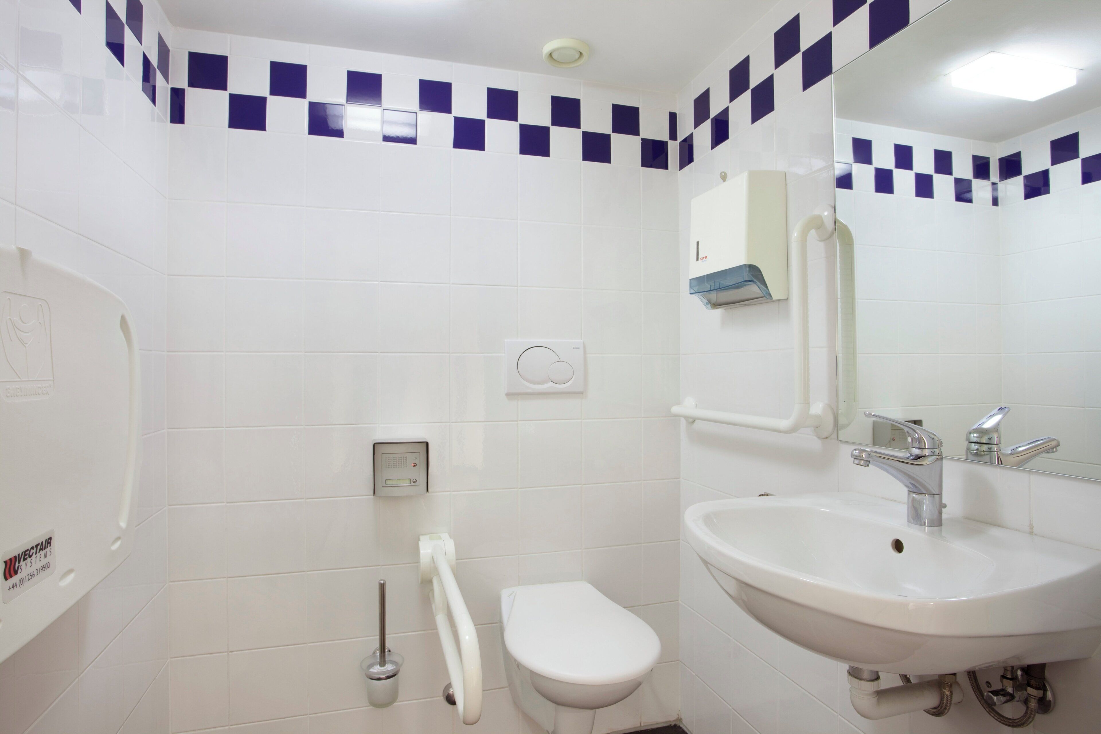 Une salle de bain avec un lavabo blanc, des toilettes et un sèche-mains.