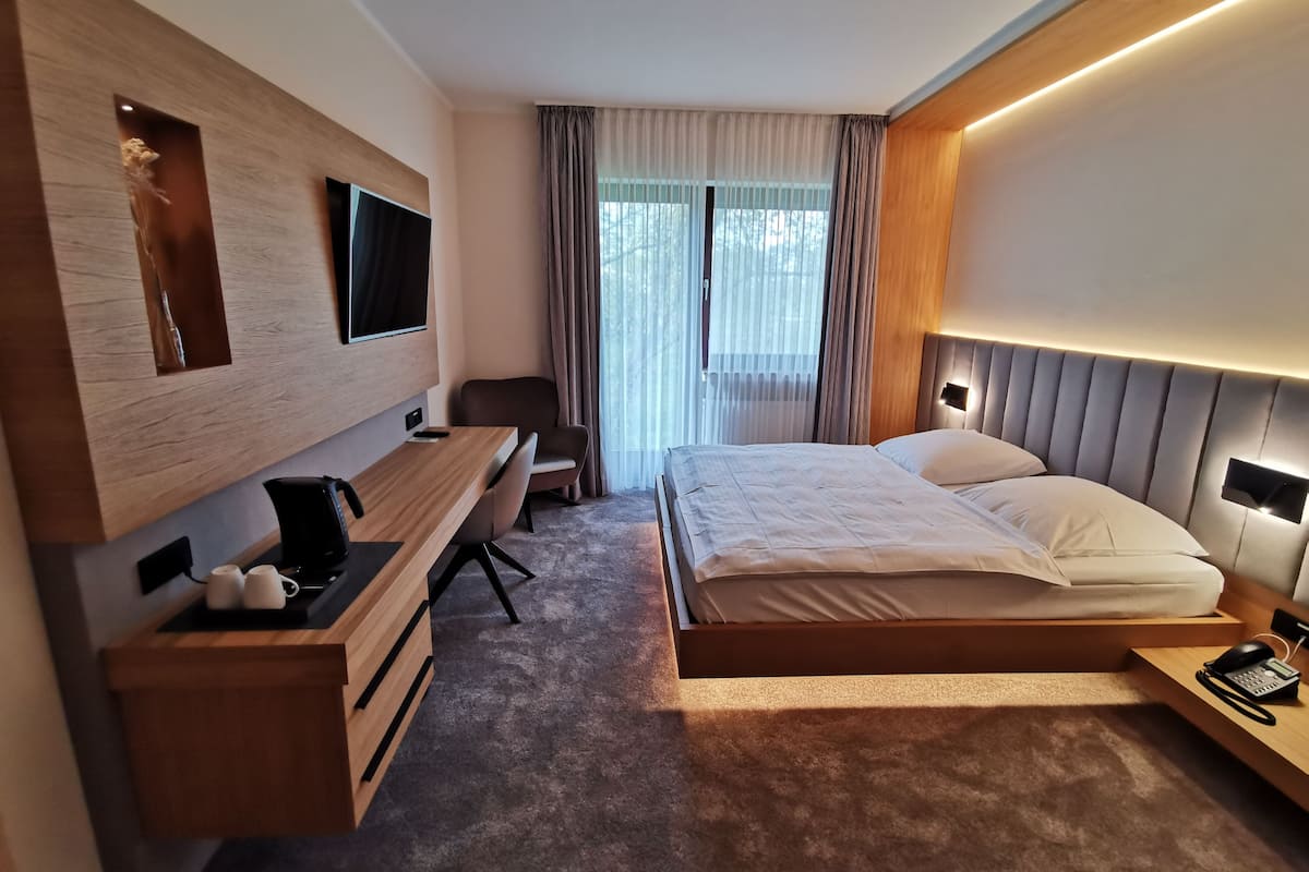 A modern hotel room with a bed, a desk, a TV, and a bedside table with a phone.
