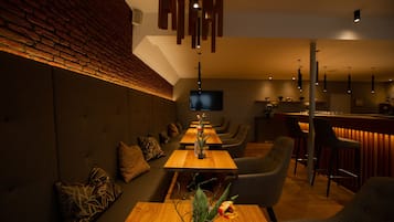 A modern bar area with wooden tables and bar stools, a flat-screen TV mounted on the wall, and a brick accent wall.