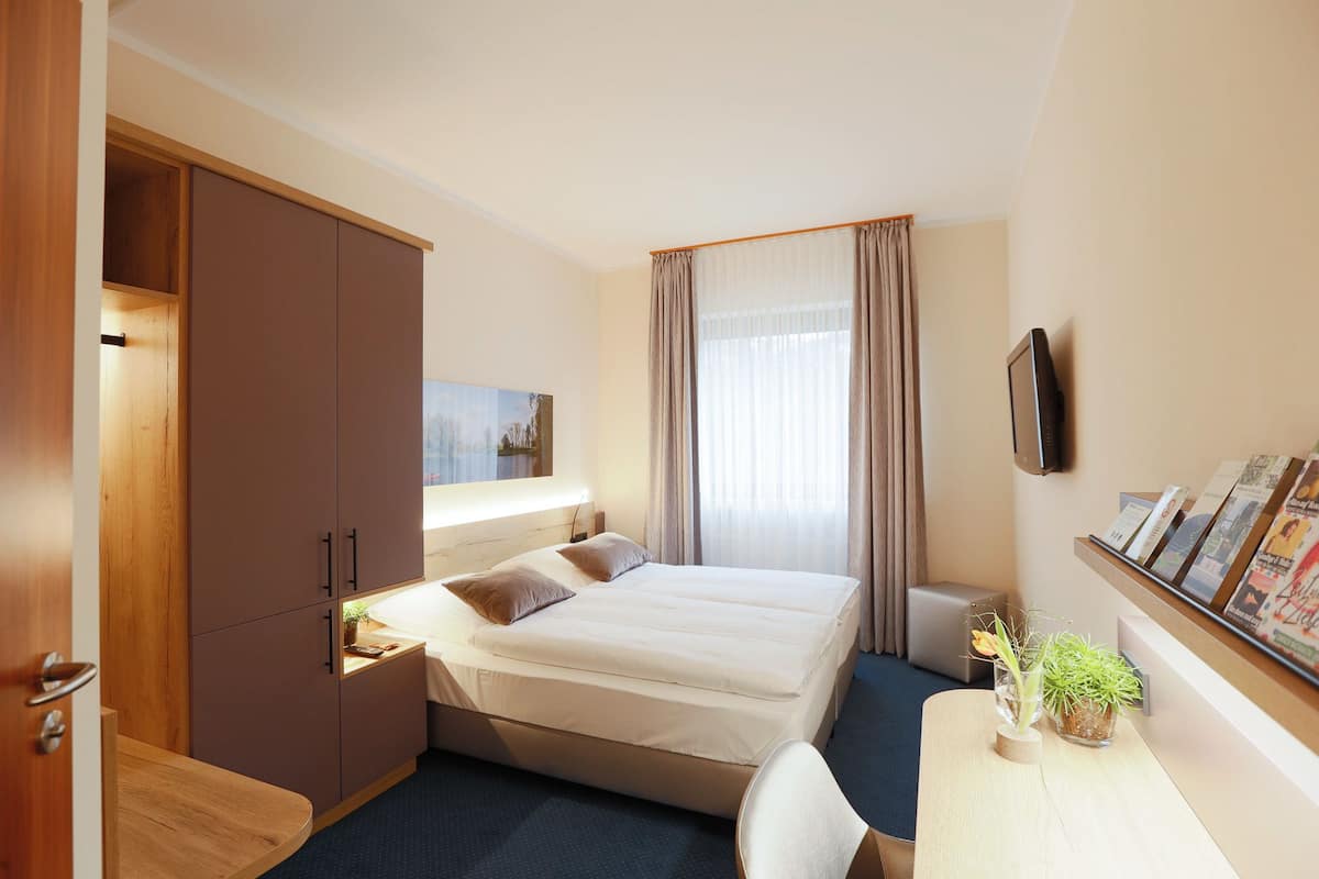 A hotel room with a bed, bedside table, lamp, and a TV mounted on the wall.
