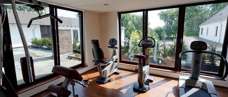 A gym with various exercise equipment, large windows, and a view of the outside.