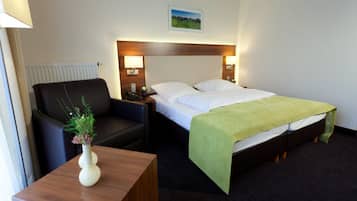A hotel room with a bed, a chair, a nightstand, a lamp, and a small table with a vase.