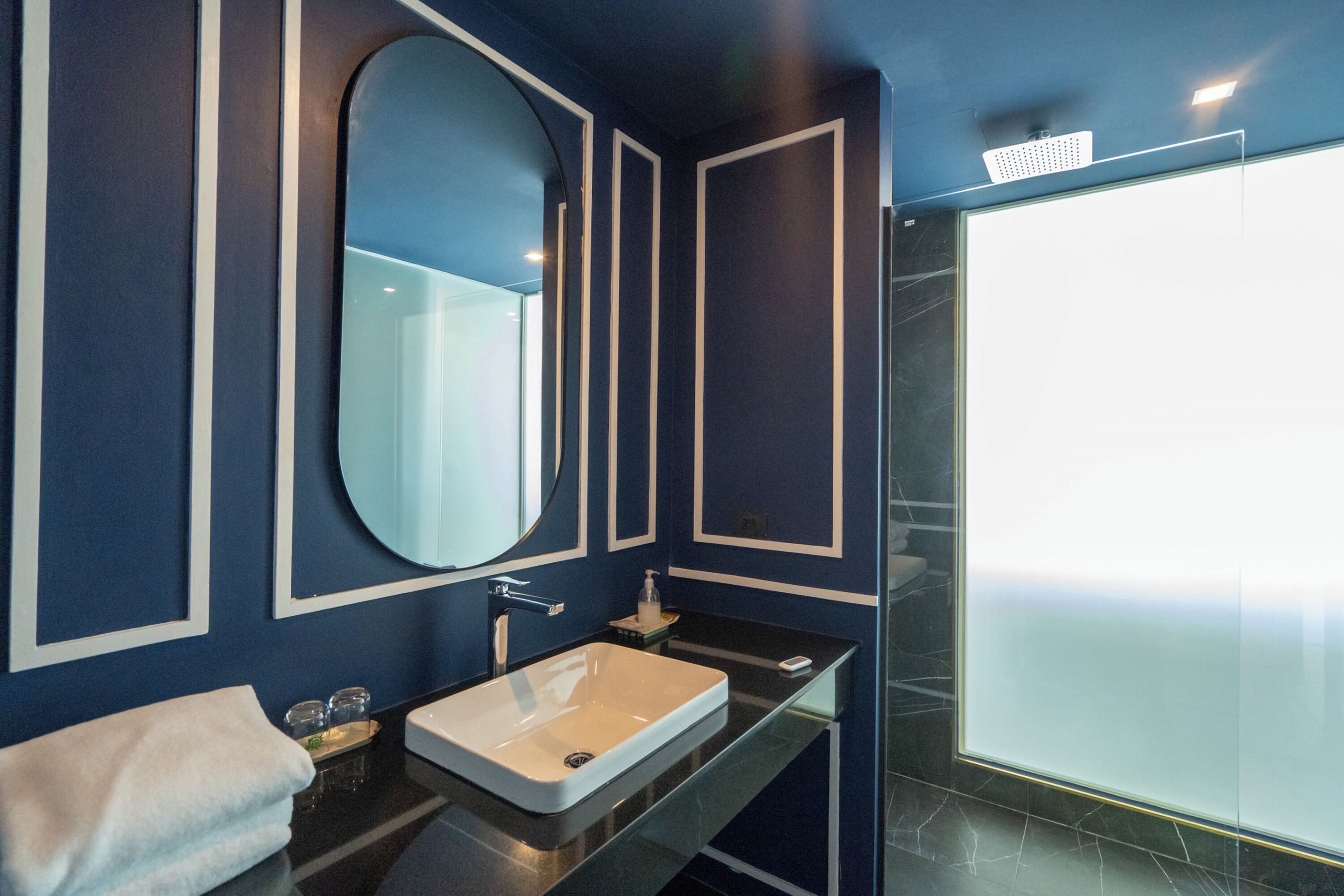 Un baño moderno con un espejo grande, un lavamanos blanco y una cabina de ducha de vidrio.