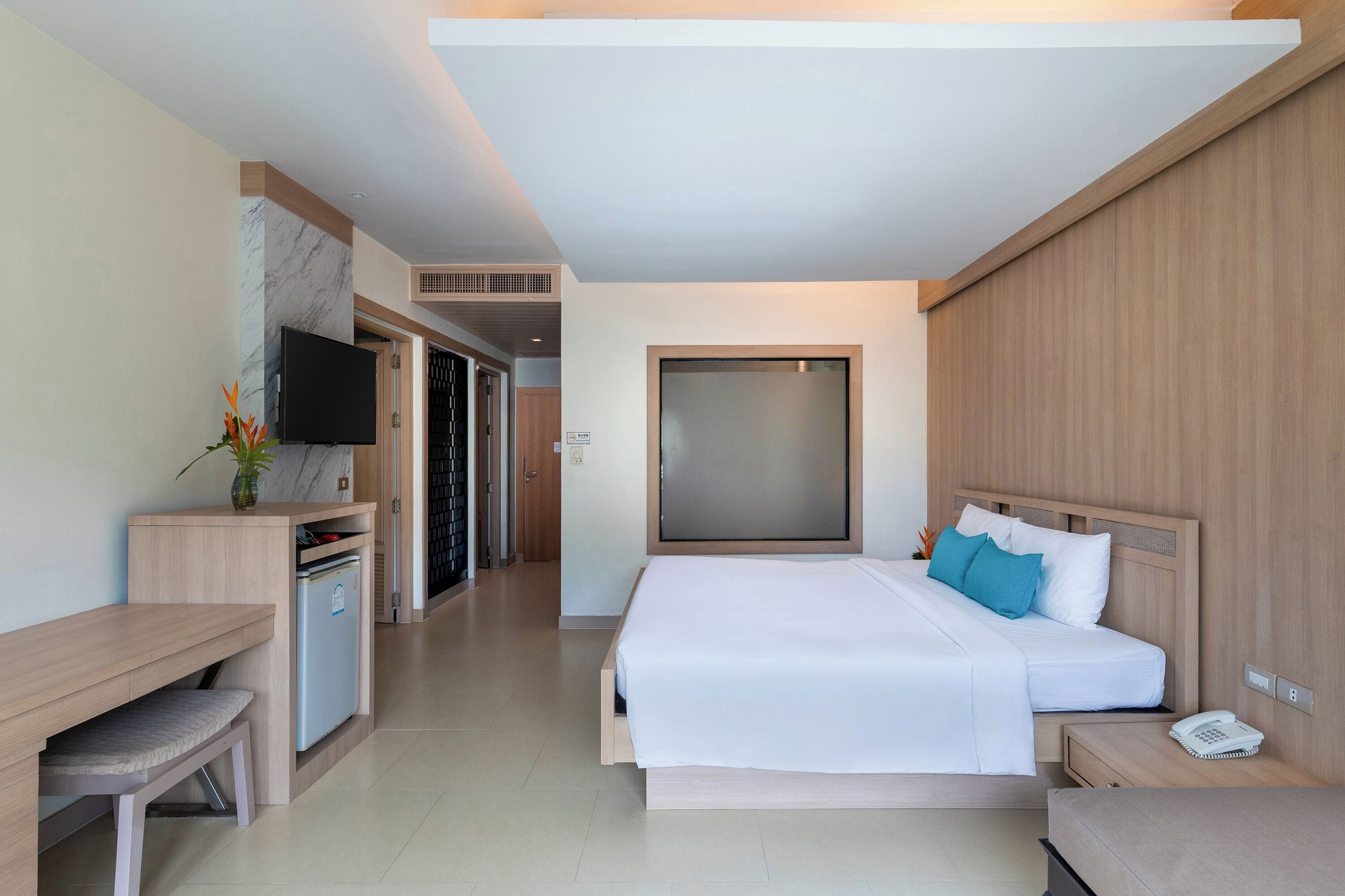 A modern hotel room with a large bed, a desk, a small fridge, and a TV.