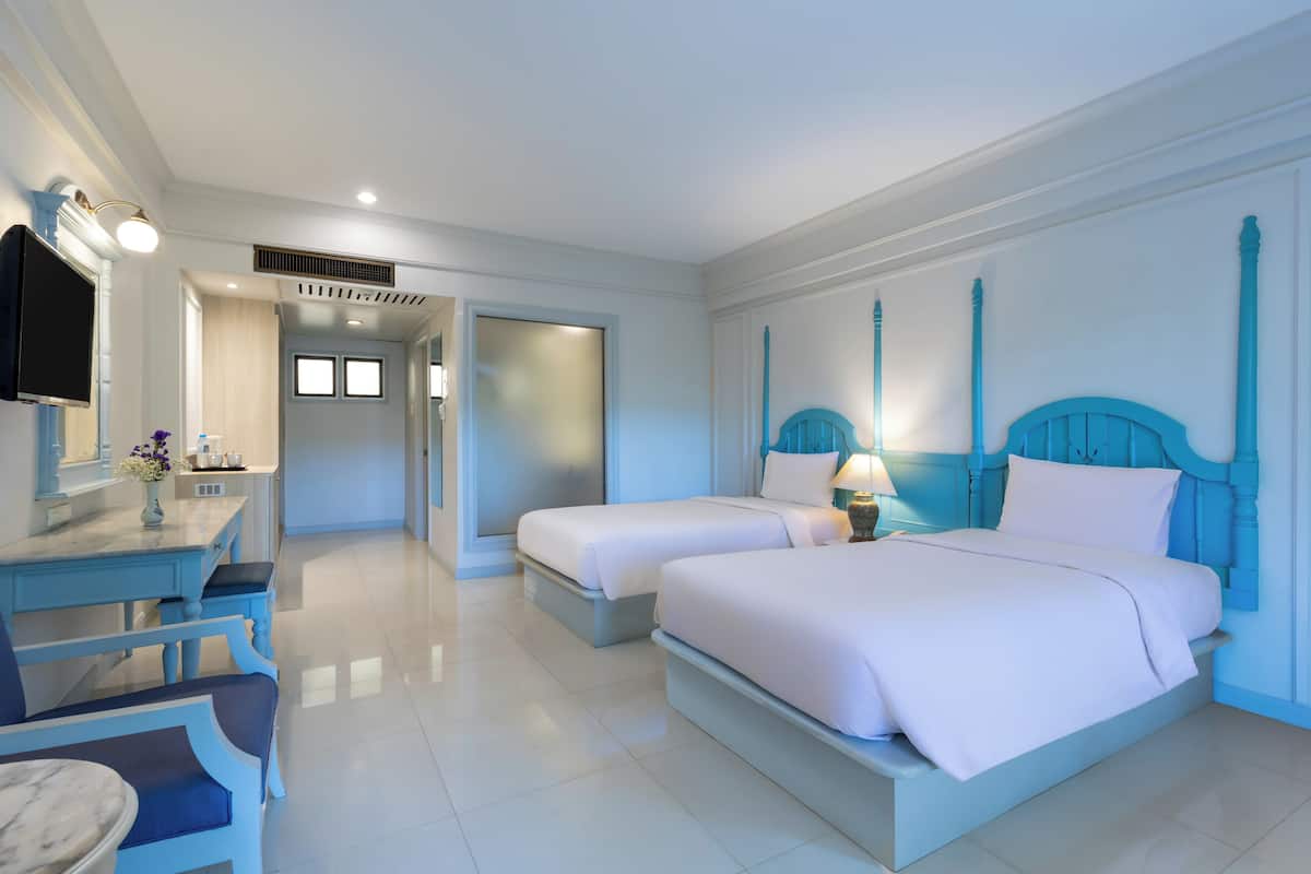 Ein Hotelzimmer mit zwei Betten, einem Schreibtisch mit Stuhl, einem Fernseher und einem durchgegangenen Türspalte sichtbaren Badezimmer.