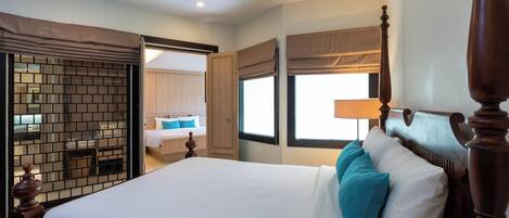 A hotel room with a large bed, a wooden headboard, a window with a view, and a door leading to another room.