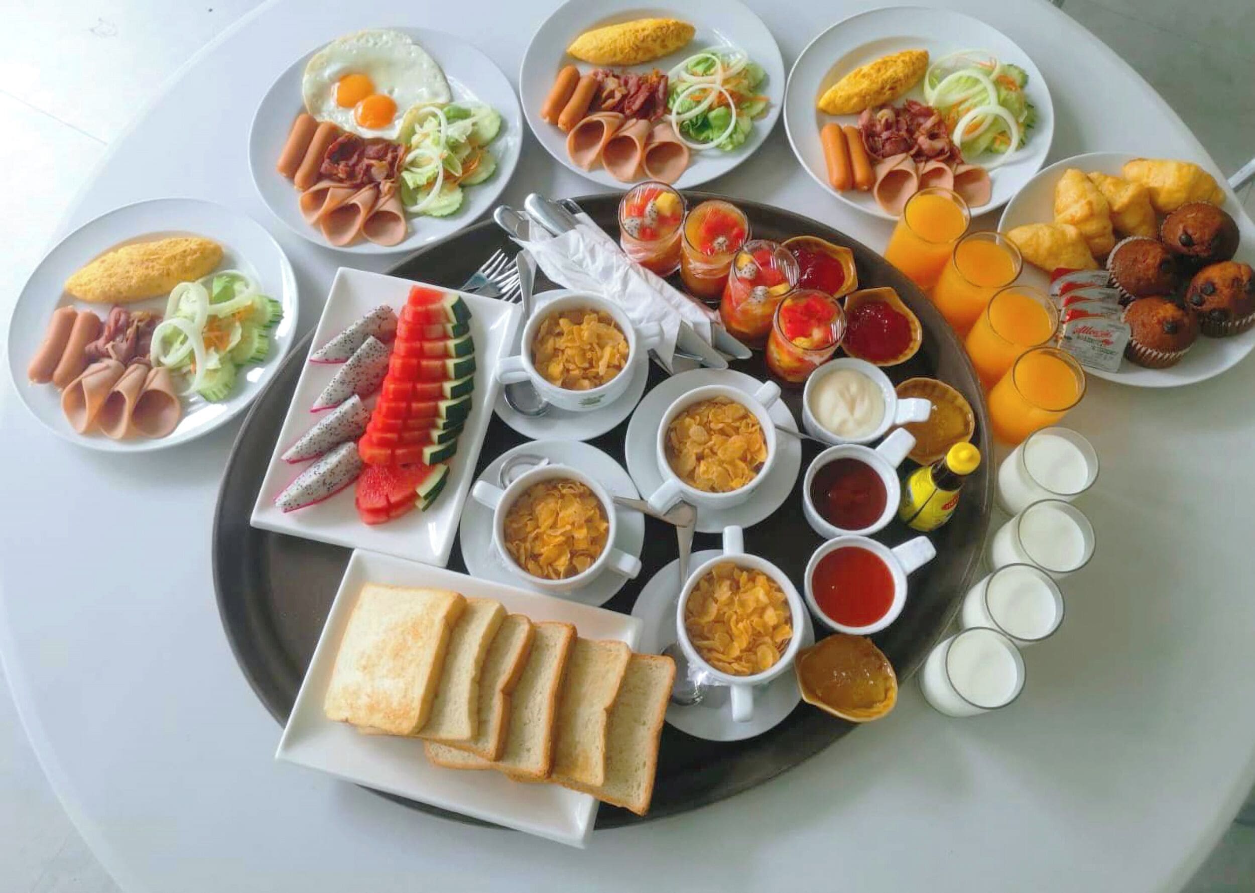 A breakfast buffet with various dishes, including eggs, meats, fruits, and beverages.