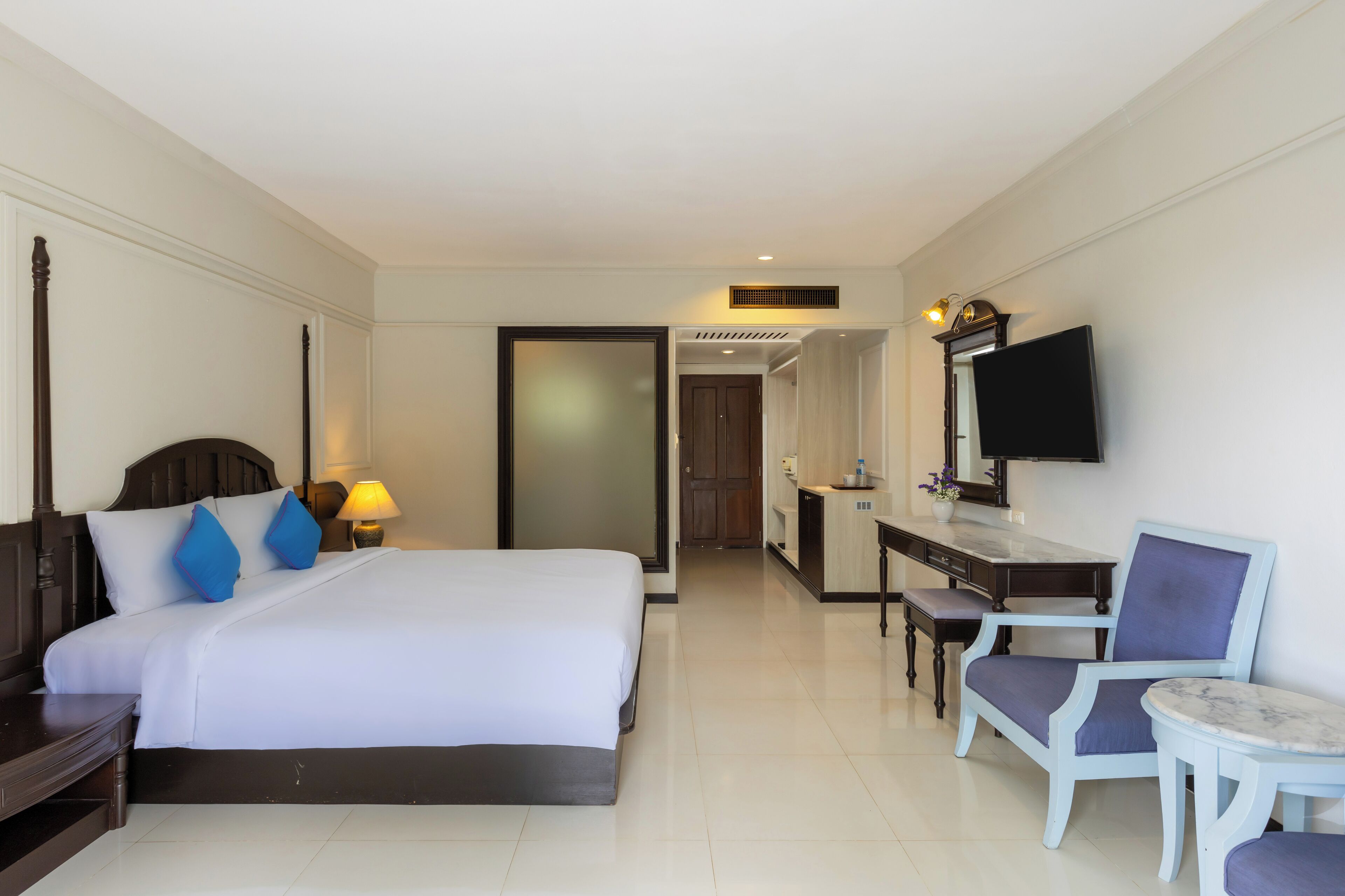 A hotel room with a large bed, a desk with a chair, a television, and a small table.