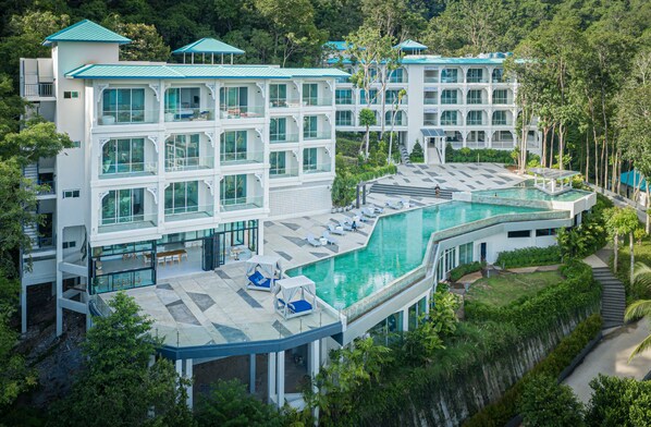 Un resort moderno con una piscina grande, varios balcones y exuberante vegetación.