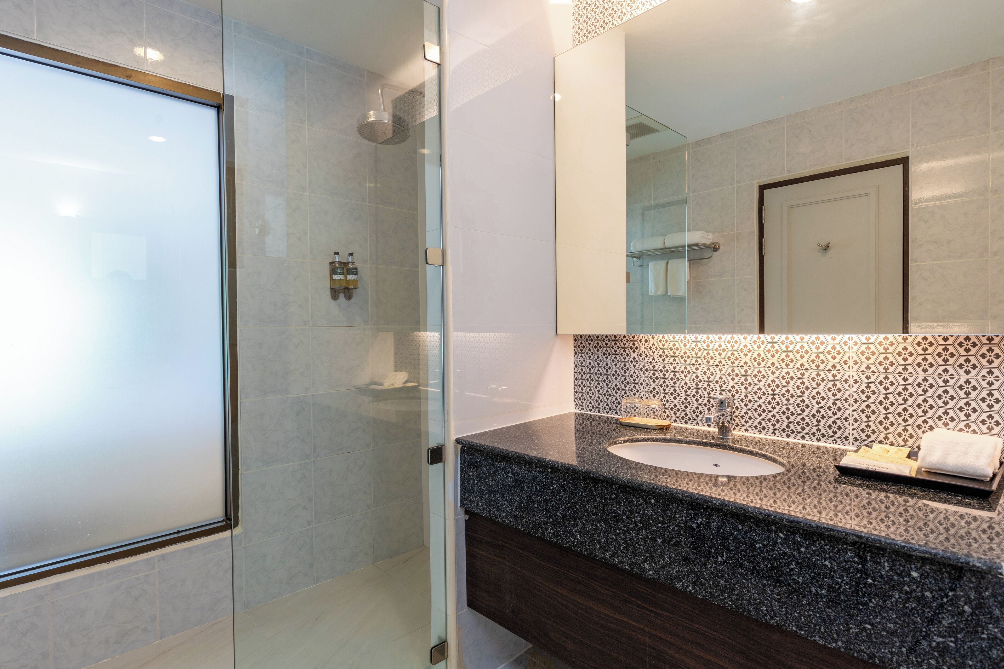 A modern bathroom with a glass shower enclosure, a granite countertop sink, and a large mirror.