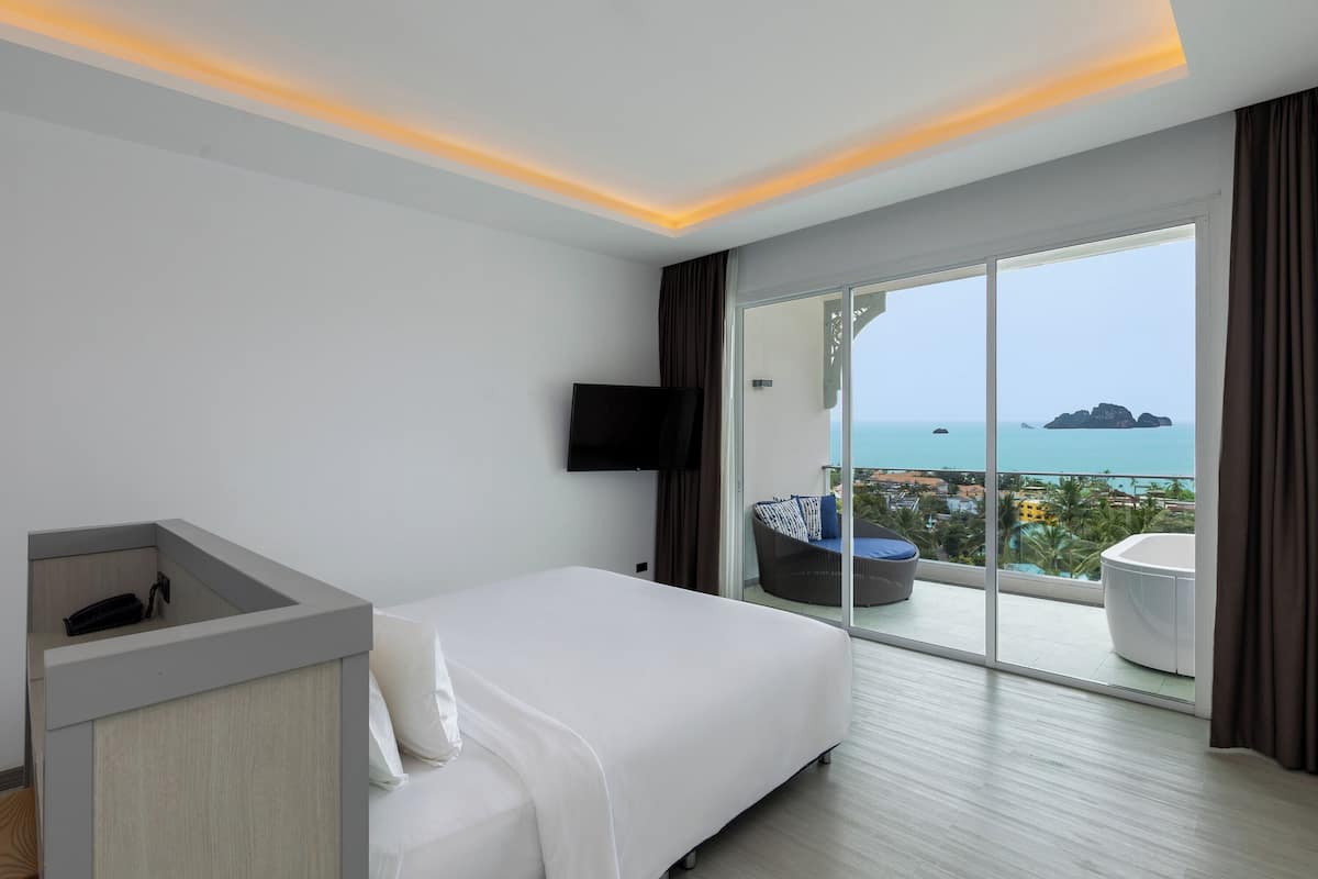 Ein modernes Hotelzimmer mit einem großen Bett, einem Schreibtisch, einem Flachbildfernseher und einem Balkon mit Meerblick.