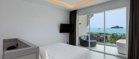 A modern hotel room with a large bed, a desk, a flat-screen TV, and a balcony with a view of the sea.