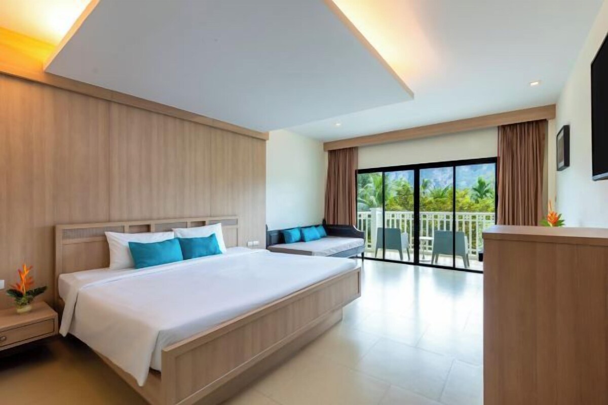 A hotel room with a large bed, a desk, and a balcony with a view.