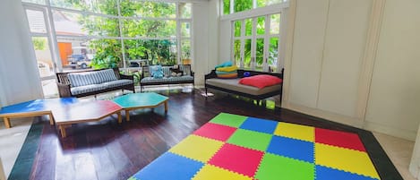 A sunlit room with large windows, a colorful foam floor, and a sofa with cushions.