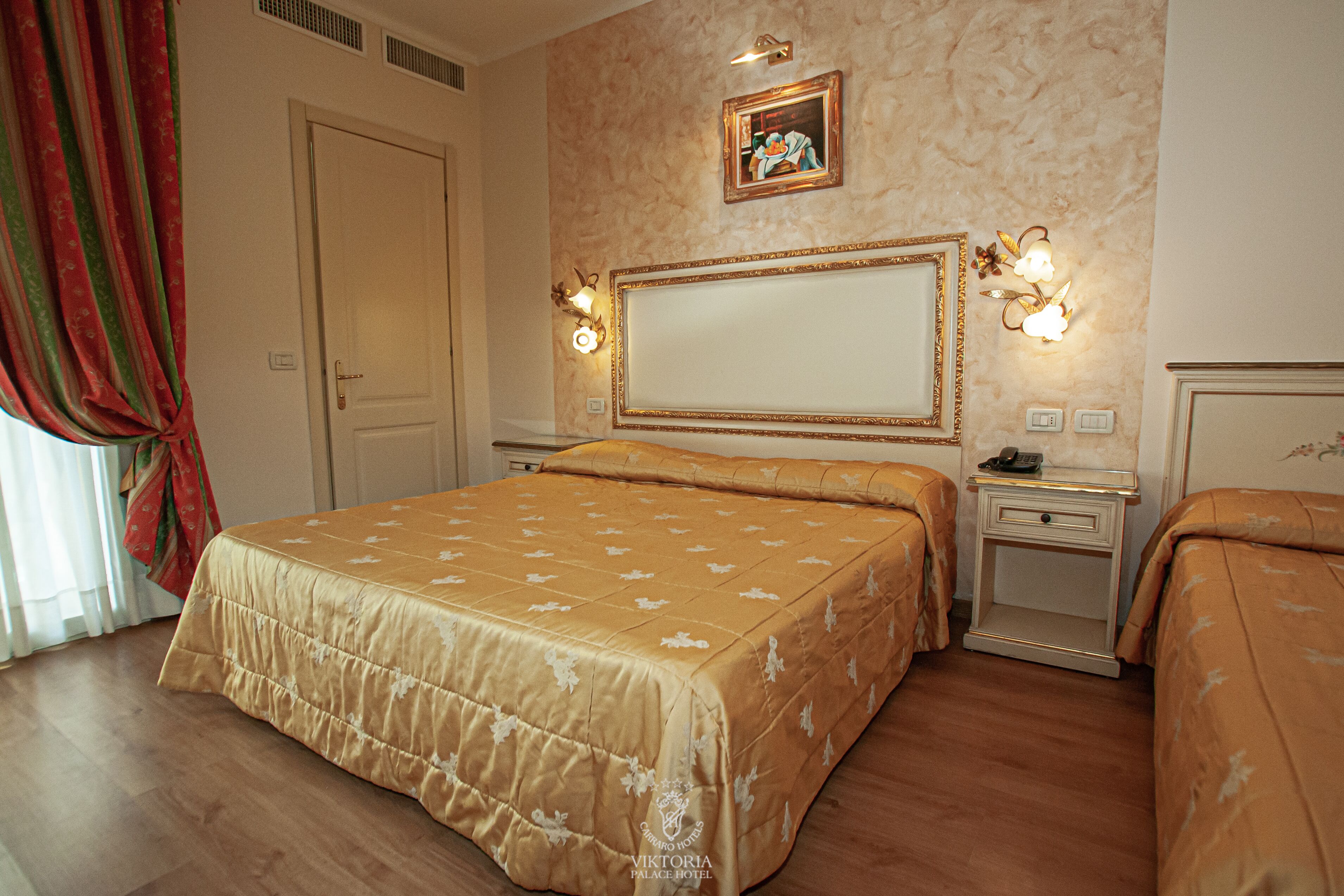 Una habitación de hotel con una cama grande, una mesita de noche con lámpara, una mesita auxiliar y un espejo montado en la pared.